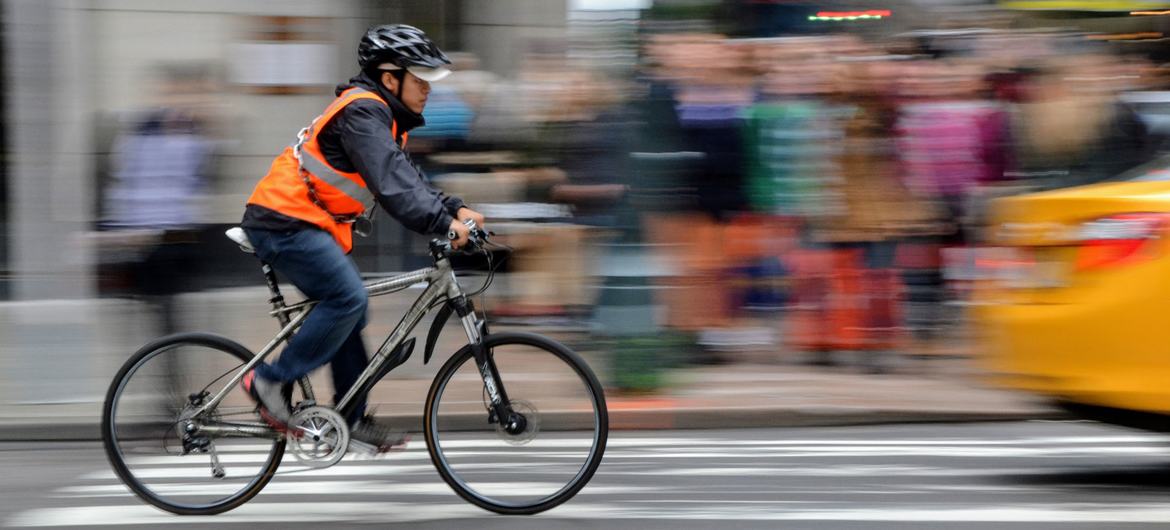 Muž nosí helmu a reflexní vestu při jízdě na kole na Manhattanu v New Yorku.